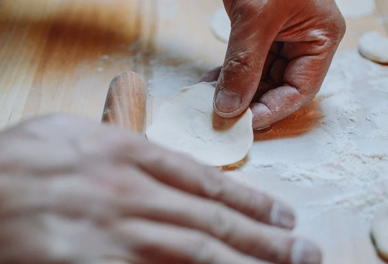 Hands folding dumplings on a floured bench